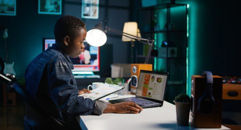 Woman working from home, writing notes on paper, looking at statistic charts